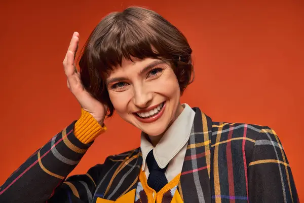 Happy college girl with short hair posing in her uniform on orange background, high school — Stock Photo