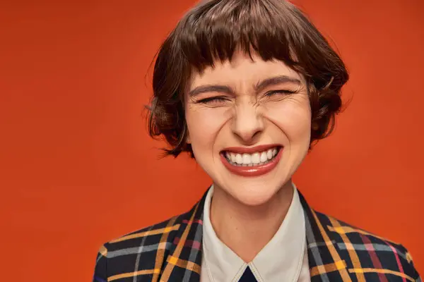 Chica universitaria alegre con una sonrisa radiante que muestra sus dientes blancos en el vibrante fondo naranja - foto de stock