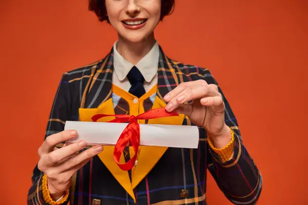 Ritagliato felice ragazza del college in uniforme a scacchi possesso diploma di laurea su sfondo arancione — Foto stock