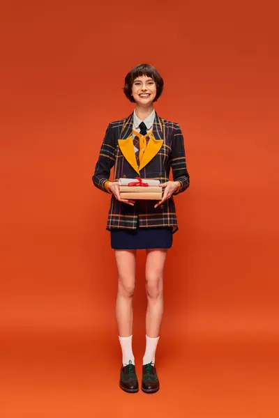 Full length of positive student in college uniform standing with books on orange background — Stock Photo