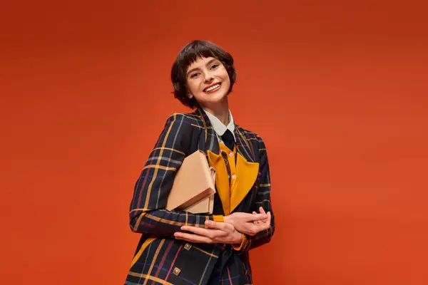 Portrait of happy student in college uniform standing with books on orange background, knowledge — Stock Photo