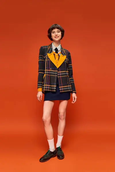 Piena lunghezza di college girl in giacca a scacchi e calzature con calzini in posa su sfondo arancione — Foto stock