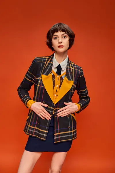 Belle collégienne en uniforme à carreaux souriant sur fond orange, vie étudiante heureuse — Photo de stock