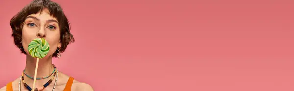 Bannière de jeune femme en tricot orange débardeur couvrant la bouche avec sucette sucrée sur fond rose — Photo de stock