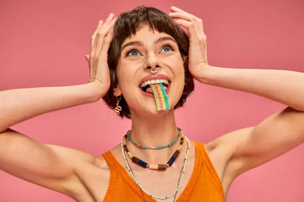 Glückliche junge Frau schmeckt süß-saure Bonbonstreifen auf der Zunge, rosa Hintergrund — Stockfoto