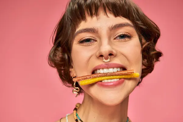 Закрыть счастливую женщину в возрасте 20 лет со сладкими и кислыми конфетками в белых зубах на розовом фоне — стоковое фото