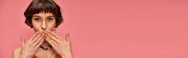 Jolie femme avec piercing du nez et cheveux bruns courts envoyant un baiser d'air sur fond rose, bannière — Photo de stock