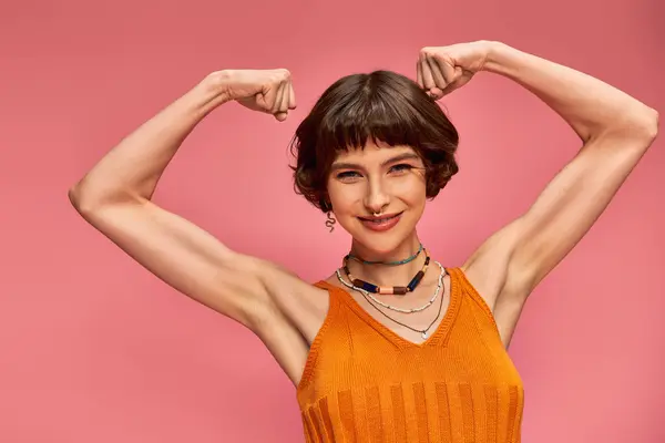 Confident young woman with piercing flexing, showing her muscles and strength on pink background — Stock Photo