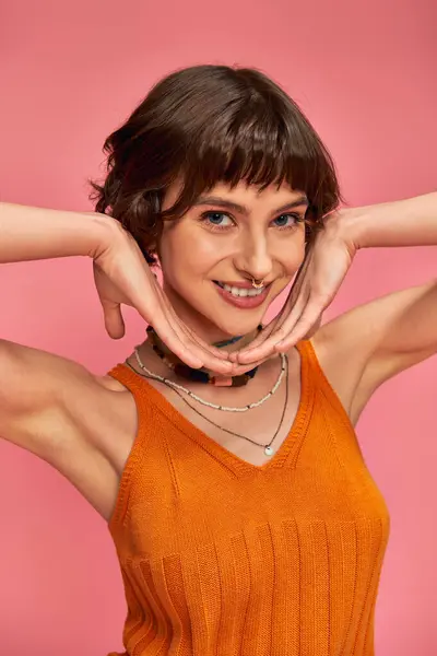 Cheerful young woman with short brunette hair in vibrant summer attire laughing on pink backdrop — Stock Photo