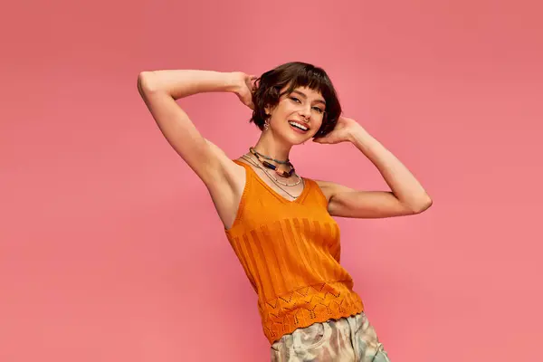 Happy young woman with short brunette hair in vibrant summer attire laughing on pink backdrop — Stock Photo