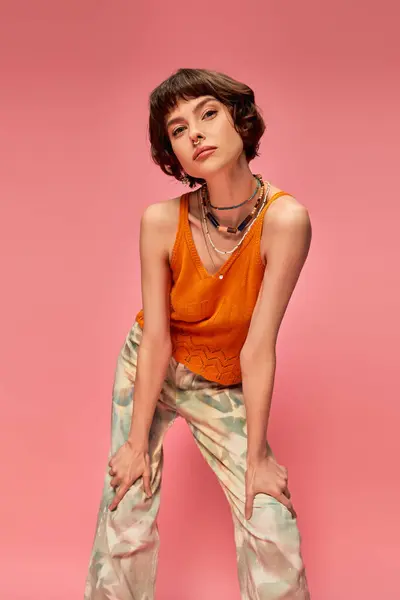 Young woman in her 20s with short brunette hair posing in vibrant summer attire on pink backdrop — Stock Photo