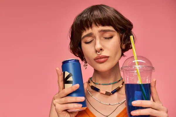 Young woman with short brunette hair and closed eyes holding blue summer drinks on pink backdrop — Stock Photo