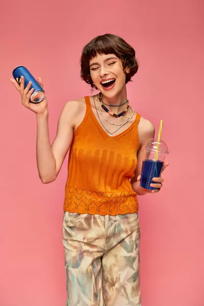 Jolly young woman with short brunette hair and piercing holding blue summer drinks on pink backdrop — Stock Photo