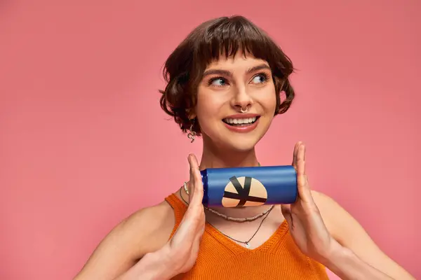 Happy young woman with short brunette hair and piercing holding soda can on pink, summer drink — Stock Photo