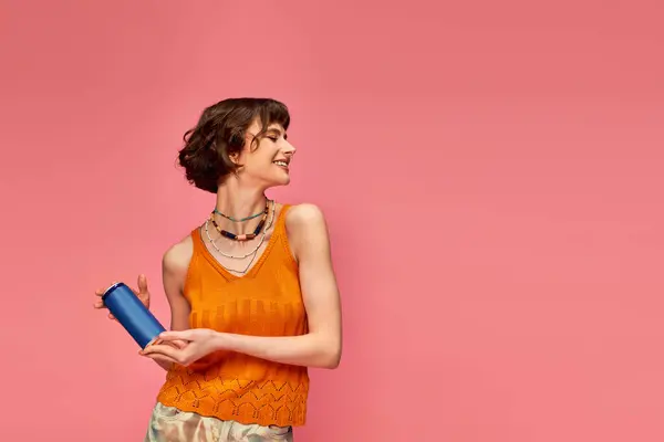 Cheerful young woman with short brunette hair and piercing holding soda can on pink, summer drink — Stock Photo