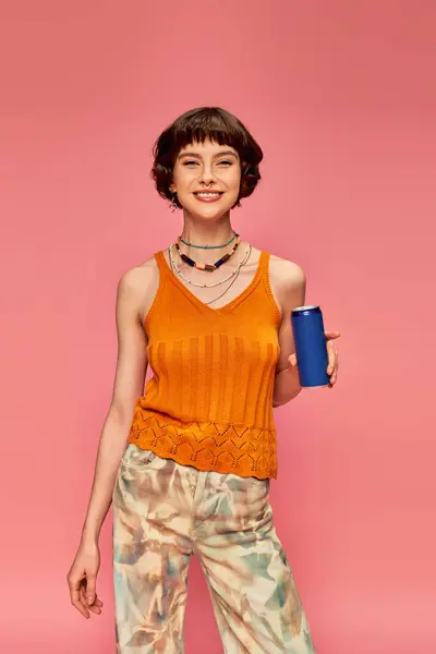 Happy young woman with short brunette hair holding soda can while posing on pink, summer beverage — Stock Photo