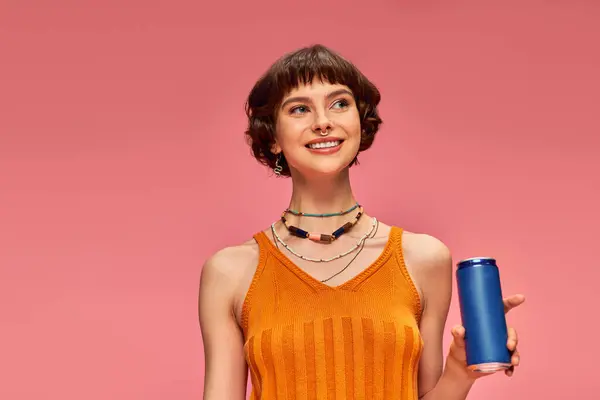 Alegre joven mujer con pelo corto morena sosteniendo soda lata mientras posando en rosa, bebida de verano - foto de stock