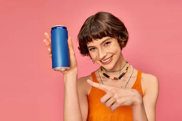 Joyful young woman with short brunette hair pointing at soda can on pink, summer beverage — Stock Photo