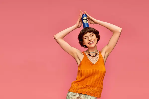 Joyful young woman with short brunette hair posing with soda can on her head on pink, summer drink — Stock Photo