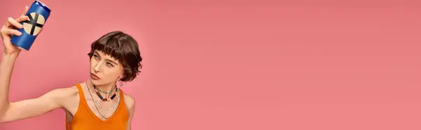 Dudosa mujer joven con pelo corto morena mirando lata de refresco en rosa, bandera de la bebida de verano - foto de stock