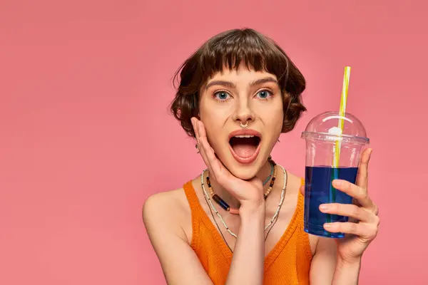 Amazed young woman with short brunette hair posing with refreshing summer cocktail on pink — Stock Photo