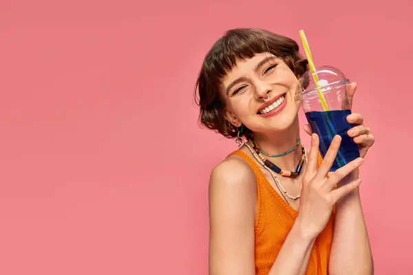 Cheerful young woman with short brunette hair posing with refreshing summer cocktail on pink — Stock Photo