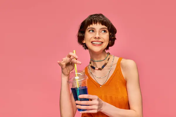 Pleased young woman with short brunette hair holding refreshing summer drink on pink backdrop — Stock Photo