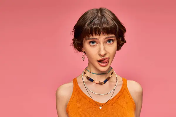 Cheeky playful girl in 20s with short brunette hair sticking tongue out on pink background — Stock Photo