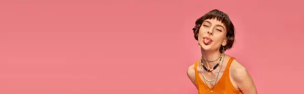 Freches verspieltes Mädchen in den 20er Jahren mit kurzen brünetten Haaren, die Zunge auf rosa Hintergrund ausstreckt, Banner — Stockfoto