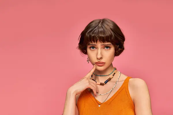 Worried young woman in her 20s standing in orange knitted tank top on pink background, concern — Stock Photo