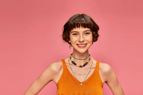 Cheerful young woman in her 20s with short hair in vibrant tank top smiling on pink background — Stock Photo