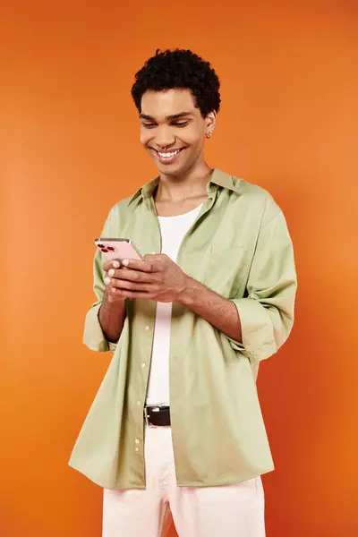 Joyous attractive african american man in cozy attire looking at his smartphone on orange backdrop — Stock Photo