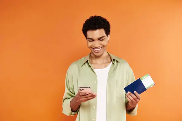 Appealing jolly african american man in cozy attire looking at phone and holding passport and ticket — Stock Photo