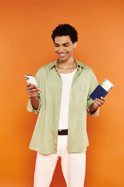 Guapo alegre afroamericano hombre en traje acogedor mirando el teléfono y la celebración de pasaporte y billete - foto de stock