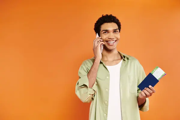 Appealing joyful african american man talking by phone and holding passport and ticket in hand — Stock Photo