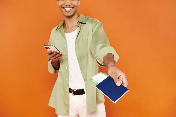 Cropped view of cheerful african american man in cozy attire holding phone and passport with ticket — Stock Photo