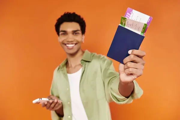 Bom olhar afro-americano alegre homem segurando telefone e passaporte com bilhete e sorrindo para a câmera — Fotografia de Stock
