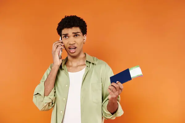 Confused appealing african american man talking by smartphone and holding passport with ticket — Stock Photo