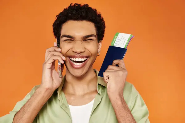 Allegro attraente uomo africano americano in abbigliamento accogliente parlando per telefono in possesso di passaporto con biglietto — Foto stock