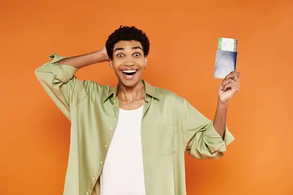 Joyful young african american man in cozy attire holding passport with ticket and smiling at camera — Stock Photo