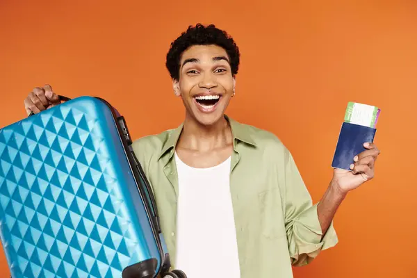 Feliz atractivo afroamericano hombre sosteniendo maleta y pasaporte con billete y sonriendo a la cámara - foto de stock