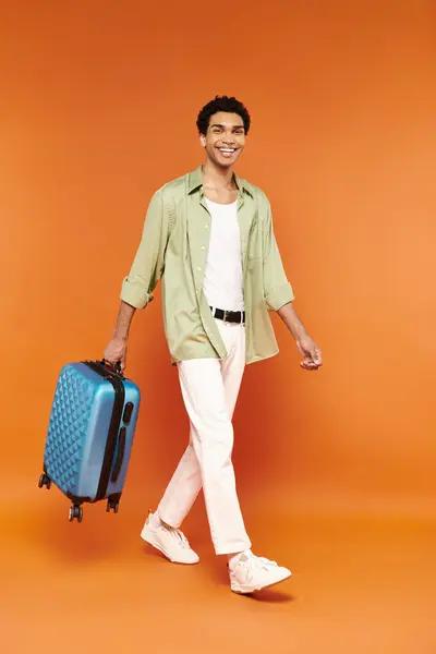 Gioioso attraente uomo africano americano in abito casual con valigia blu e sorridente alla macchina fotografica — Foto stock