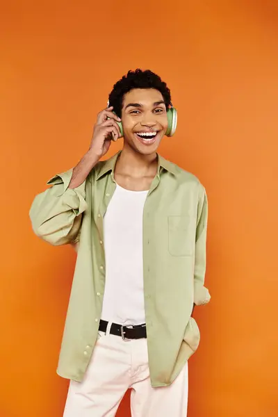 Alegre hombre afroamericano con estilo en ropa casual con auriculares y sonriendo a la cámara felizmente - foto de stock