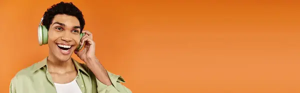 Joyous young african american man in cozy attire with headphones looking away, orange backdrop — Stock Photo