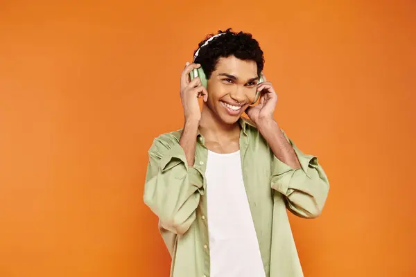 Joyful stylish african american man in cozy attire with headphones looking away, orange backdrop — Stock Photo