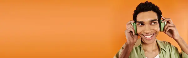 Merry african american man in cozy attire with headphones looking away, orange backdrop, banner — Stock Photo