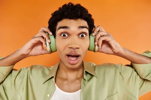 Surprised african american man in casual clothes with headphones and smiling at camera happily — Stock Photo
