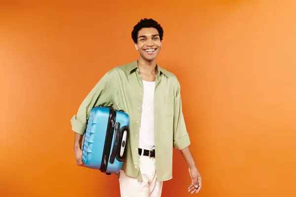 Joyous young african american man in casual clothing holding his suitcase and smiling at camera — Stock Photo