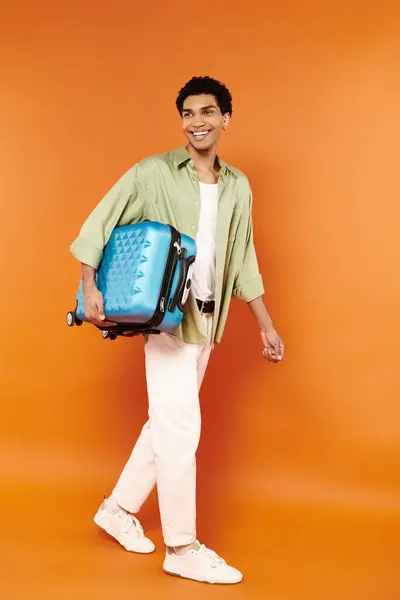 Bello allegro afro americano uomo in abbigliamento accogliente a piedi con la sua valigia blu in mano — Foto stock