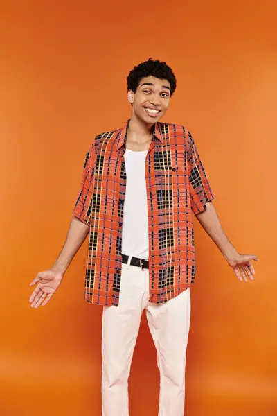 Веселий афроамериканський чоловік у яскравому одязі позує на помаранчевому тлі і дивиться на камеру — стокове фото